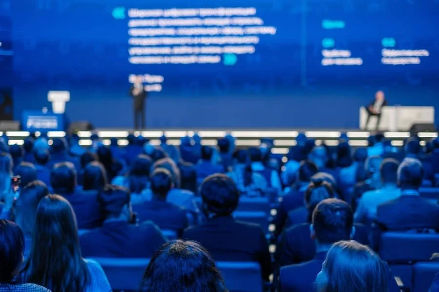 Audience watching a speaker present at a large business conference