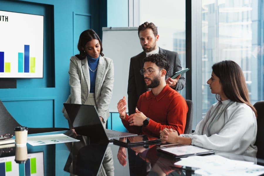 A sales metrics meeting where four people are discussing beside a laptop