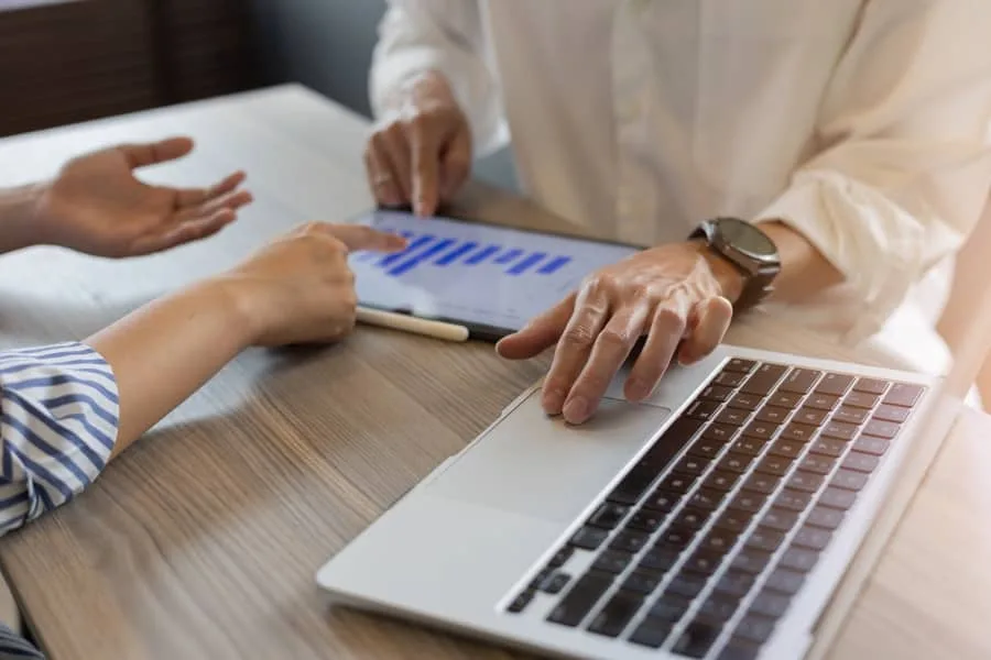 Two people reviewing data on tablet and laptop in a meeting