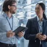 Two professionals having a discussion in a modern office environment, one holding a tablet